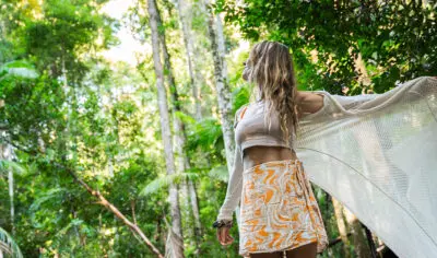 A woman standing in a rainforest looking up at the tree tops.