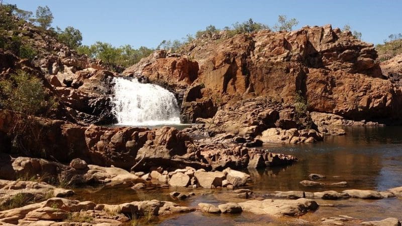 Stunning waterfall cascades into a rocky pool beneath clear blue skies, a must-see on the 10 Day Darwin to Broome 4WD Adventure.