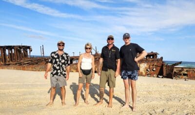 backpackers exploring K'gari at Maheno shipwreck in the background with Peterpans