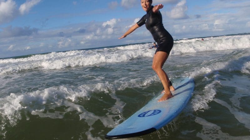 Smiling woman in wetsuit expertly surfs Australia’s Longest Wave, balancing skilfully on ocean waves beneath dramatic cloudy sky.