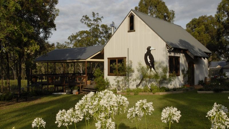 Elegant white house featuring a striking bird silhouette, set among lush trees and vibrant white flowers—ideal for Hunter Valley wine tours.