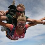 Two people tandem skydiving over Sydney, smiling and giving thumbs up above the clouds—experience top-rated Skydive Extras.
