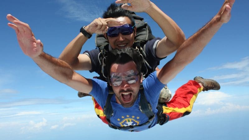 Experience the thrill of Skydive Sydney tandem skydiving—two men smile mid-air, goggles on, soaring in a vibrant blue sky.