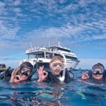 Three scuba divers signal OK underwater near a dive boat during a PADI Rescue Diver Course, demonstrating safe scuba diving skills.