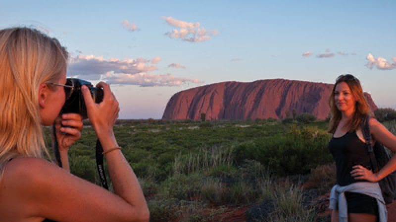 Two women photographing iconic Uluru at sunset on a 3-night adventure tour from Alice Springs to Yulara in Australia’s Red Centre.