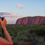 Two women photograph iconic Uluru on a 3-night Rock The Centre Yulara adventure, with dramatic clouds enhancing the Outback landscape.