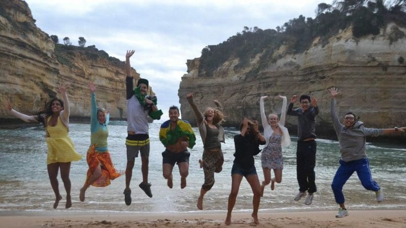 Group of eight people leaps with excitement on a scenic beach during a 1 Day Great Ocean Road 12 Apostles Tour by Go West Tours.