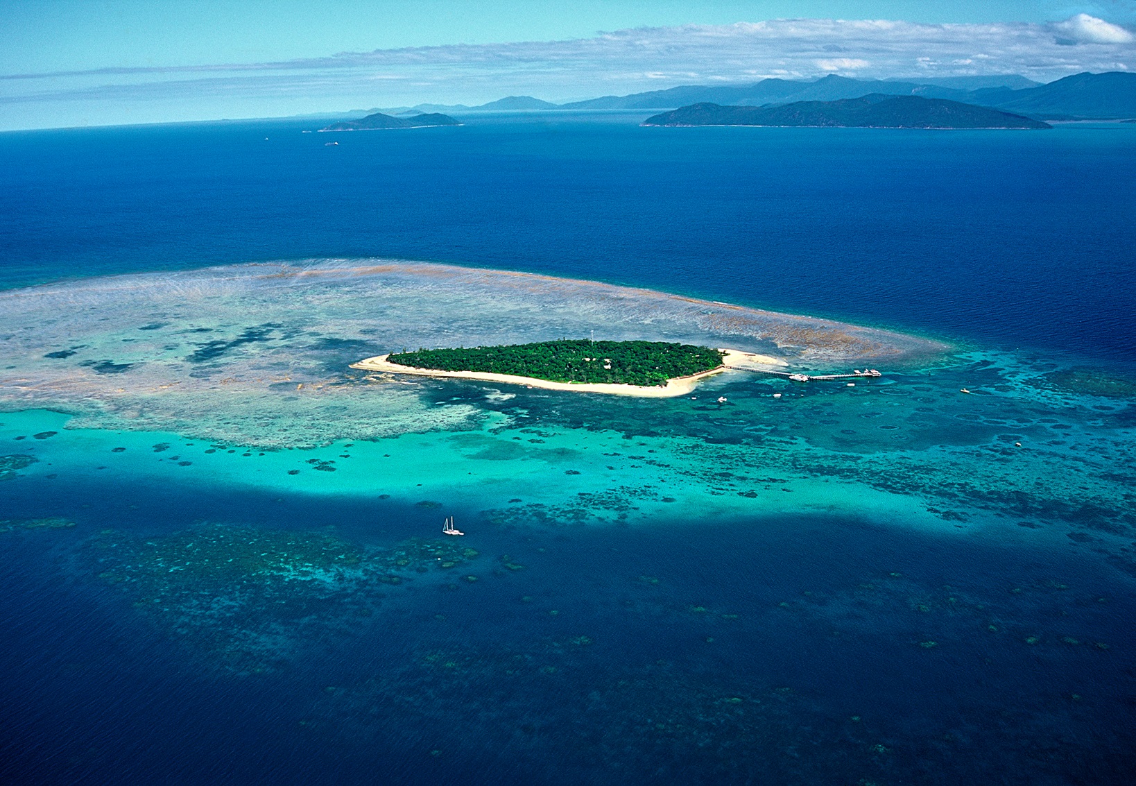 Experience a breathtaking aerial view of a lush green island, vibrant coral reefs, and turquoise waters on a Great Barrier Reef flight.