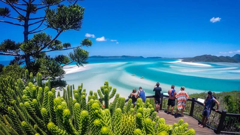 Visitors enjoy panoramic views from a wooden lookout deck above pristine white sand beaches and crystal-clear turquoise water below.