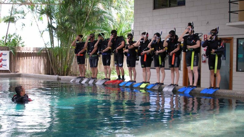 Participants get ready to enter the swimming pool for a 1 Day PADI Refresher Course, closely supervised by their expert diving instructor nearby.