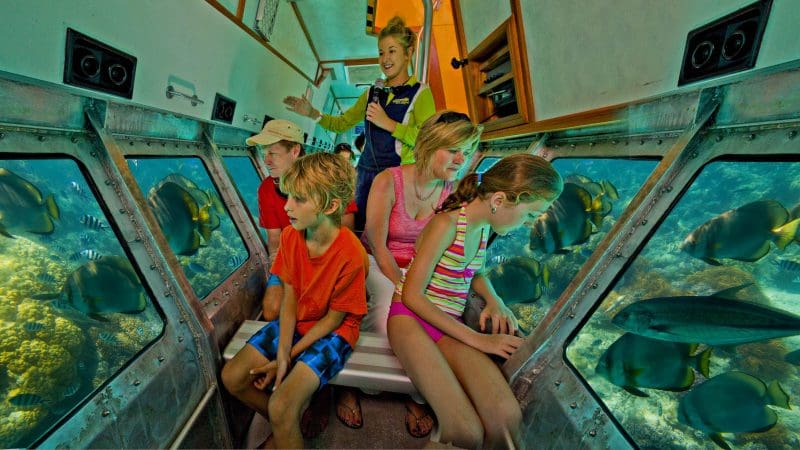 Family explores vibrant marine life and colourful coral reefs from a semi-submarine on a Half Day Green Island tour in crystal waters.