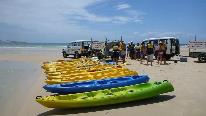 Vibrant kayaks lined up on Rainbow Beach for the Dolphin Kayaking Great Beach Drive Adventure under clear blue Queensland skies.