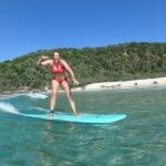 Woman in a vibrant red bikini expertly surfs crystal-clear blue waves at Learn to Surf Australia's renowned Longest Wave Beach Drive.