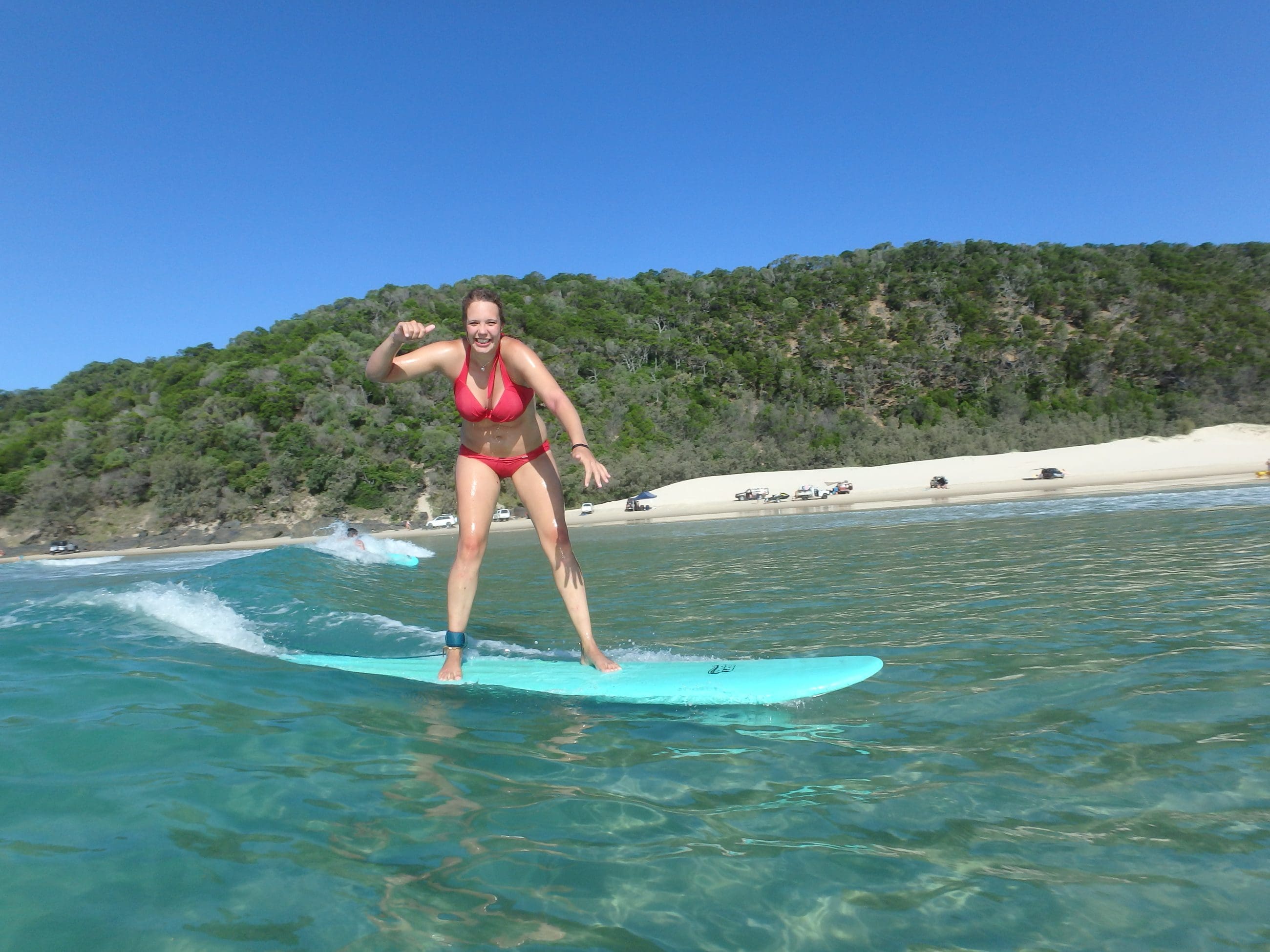 Woman in a vibrant red bikini expertly surfs crystal-clear blue waves at Learn to Surf Australia's renowned Longest Wave Beach Drive.
