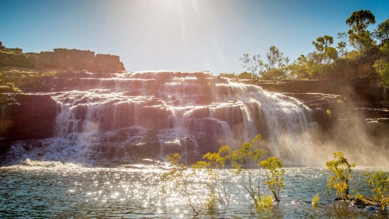 Sunlight illuminates a majestic cascading waterfall, a top attraction on the 10 Day Broome to Darwin Kimberley Off-road Adventure Tour.