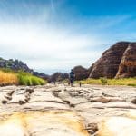 Traveller trekking across a rugged, sunlit riverbed on the 10 Day Broome to Darwin Kimberley Off Road Adventure Tours experience.