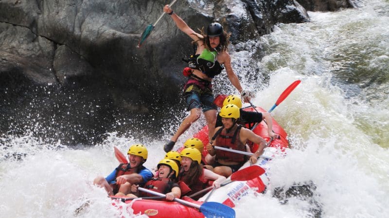 Adventure seekers in helmets and life jackets navigate thrilling Barron River rapids on a half-day white-water rafting near Cairns.