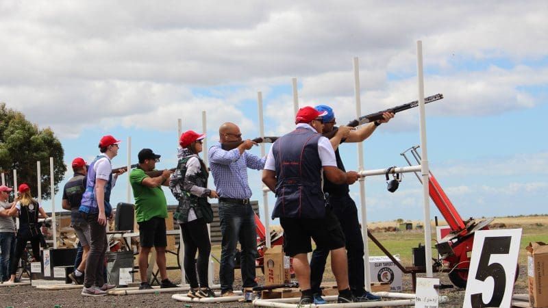 Participants wearing red caps enjoy an outdoor clay pigeon shooting event at Vic Werribee beneath a dramatic cloudy sky.