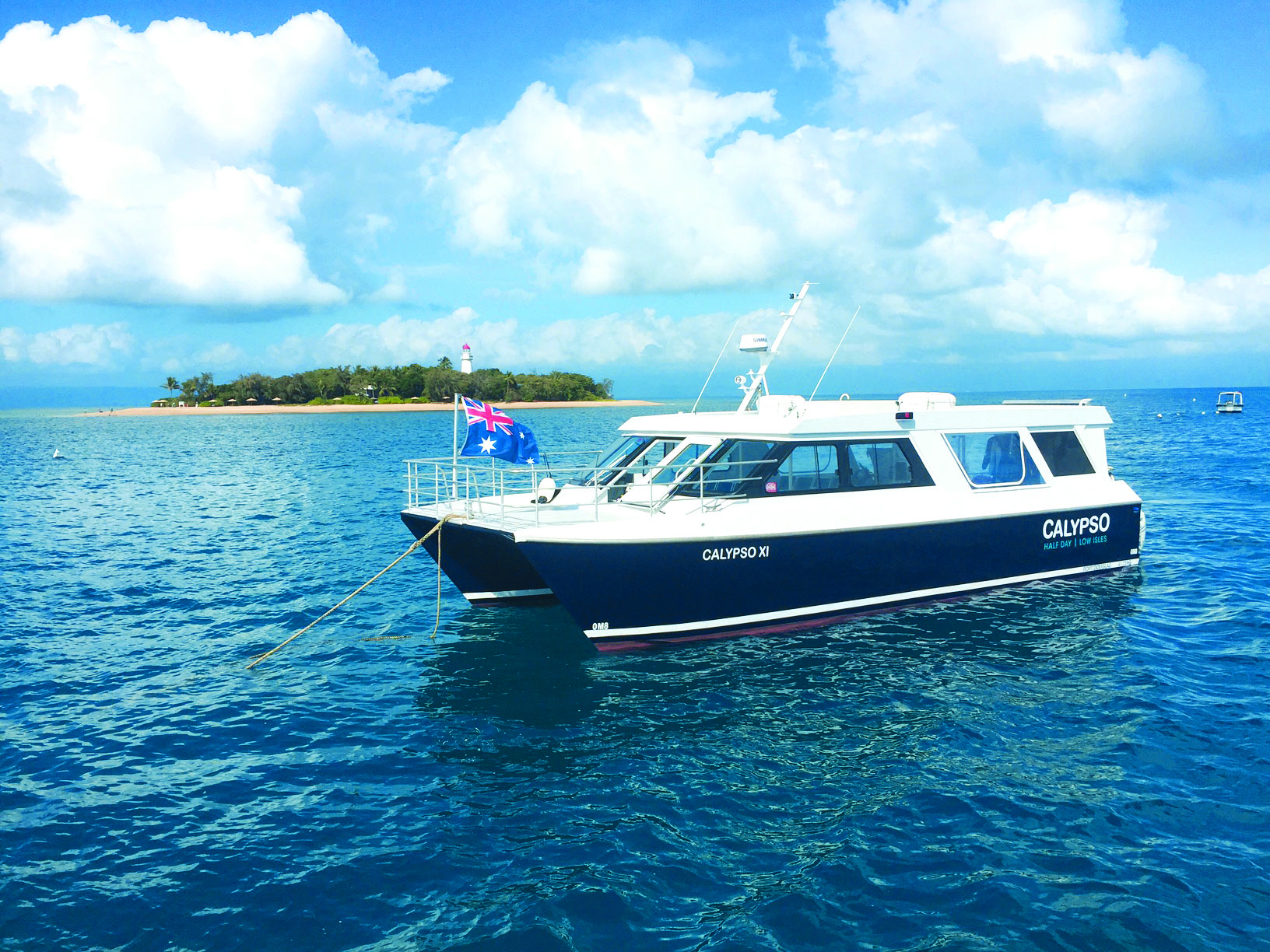 A sleek white and blue Calypso boat floats on crystal-clear waters near a tropical island—Half Day To Low Isles Reef Charters tour.