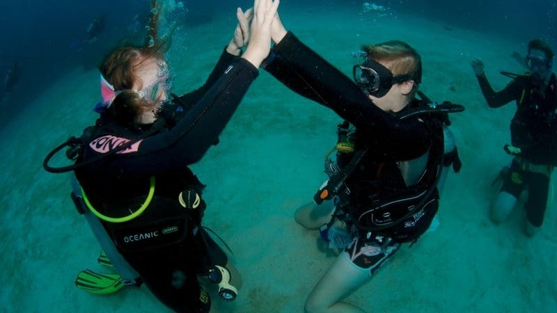 Two scuba divers high five underwater during an epic 6 Day Liveaboard PADI Advanced Open Water Course, showcasing diving skills.