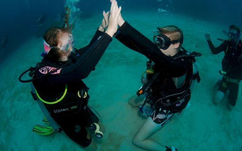 Two scuba divers high five underwater during an epic 6 Day Liveaboard PADI Advanced Open Water Course, showcasing diving skills.