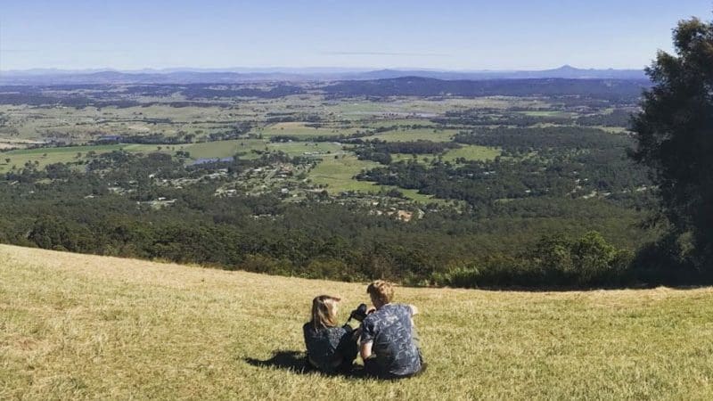 Two people relax on a lush hill overlooking the scenic Gold Coast, imagining an exclusive gourmet tasting experience and culinary delights.