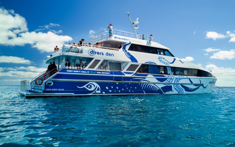 Aquaquest Outer Reef Dive: Stunning white and blue boat with ocean-inspired art floats on crystal-clear tropical water under sunny skies.