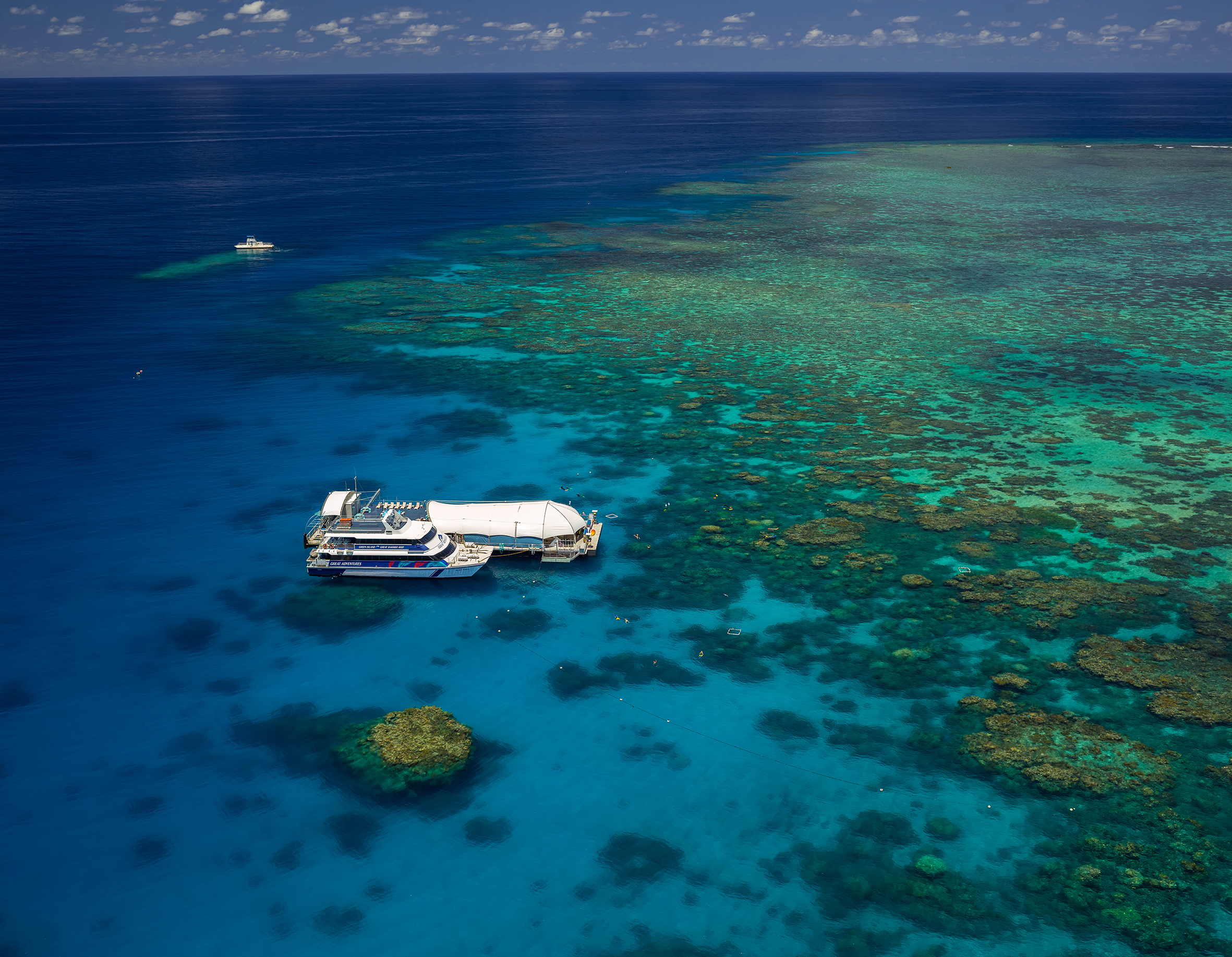 Tour boat anchored by the Great Barrier Reef Activity Platform in pristine turquoise waters beneath a vibrant, sunny sky.