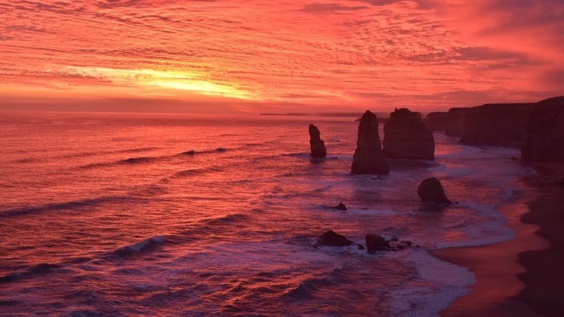 Spectacular red and orange sunset over Great Ocean Road cliffs, waves crashing below—unforgettable scenic tour on Australia’s coastline.