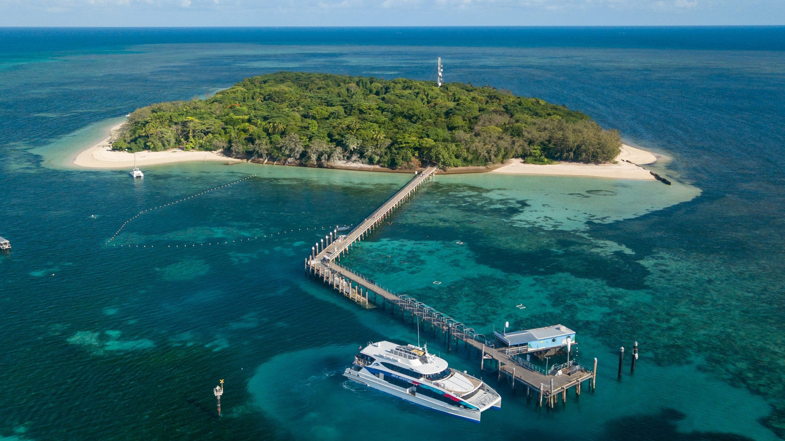 Discover a lush tropical island featuring pristine sandy beaches, a scenic pier, and the Green Island Transfers ferry on turquoise waters.