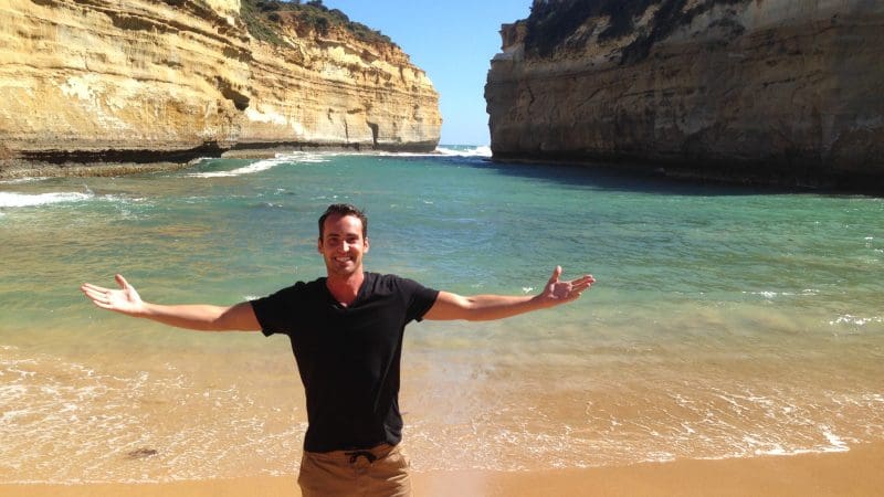 Man with arms wide open on sandy beach enjoying sunset during Go West Tours’ 1 Day Great Ocean Road Sunset Tour, stunning scenery.