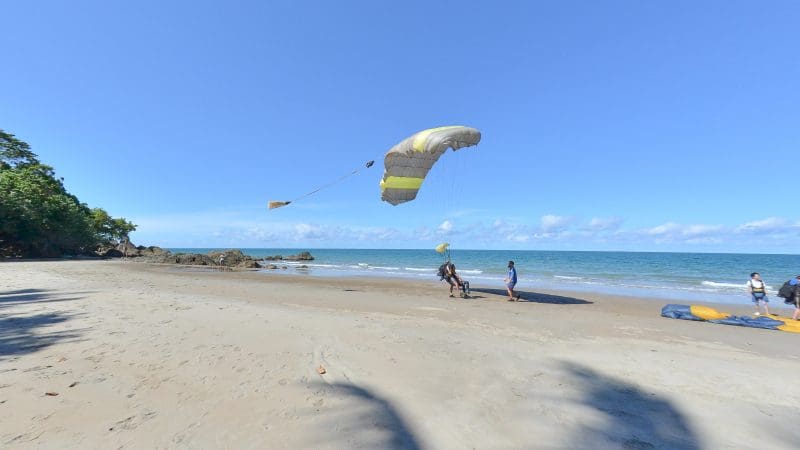 Adventurers set up a yellow and white parachute for Cairns Tandem Skydive Extras on a scenic sandy beach near the sea waves.