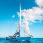Hammer 2 Day 2 Night Whitsunday Sailing group cruises crystal-clear blue waters under a vibrant sky dotted with scattered white clouds.