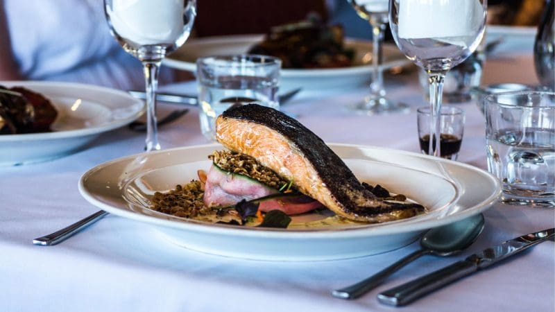 Savour a gourmet Gold Coast salmon fillet with vibrant vegetables, plated elegantly on white tablecloth for the ultimate tasting experience.