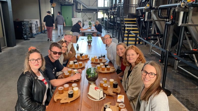 Smiling group tasting craft beer flights at a vibrant brewery during an Arvo Session Behind The Barrel Half Day Tour, posing for photo.