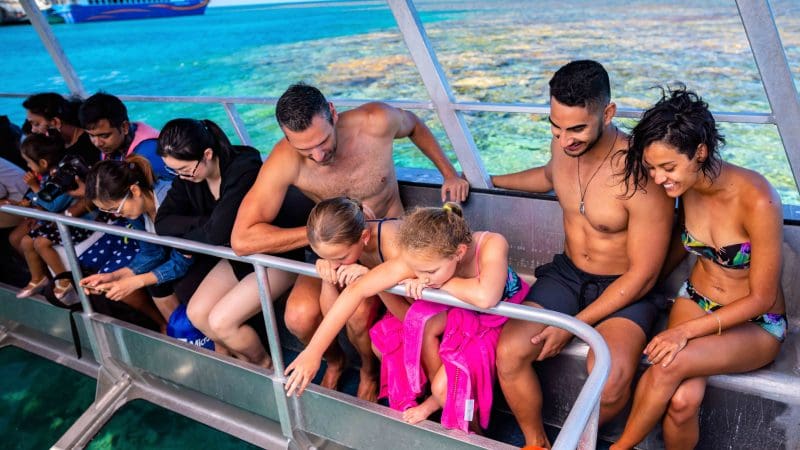 Tourists aboard a glass-bottomed boat admire vibrant coral reefs near a docked ship during a one-day Outer Reef Fitzroy Island tour.