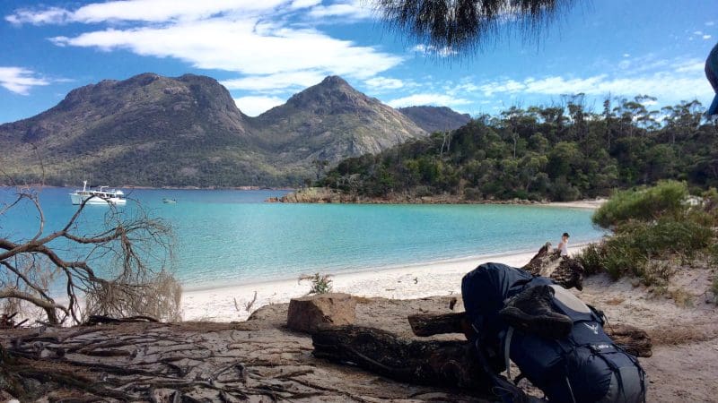Rucksack on pristine sand beside crystal-clear turquoise water at Wineglass Bay, Tasmania—full-day tour highlights near Richmond.