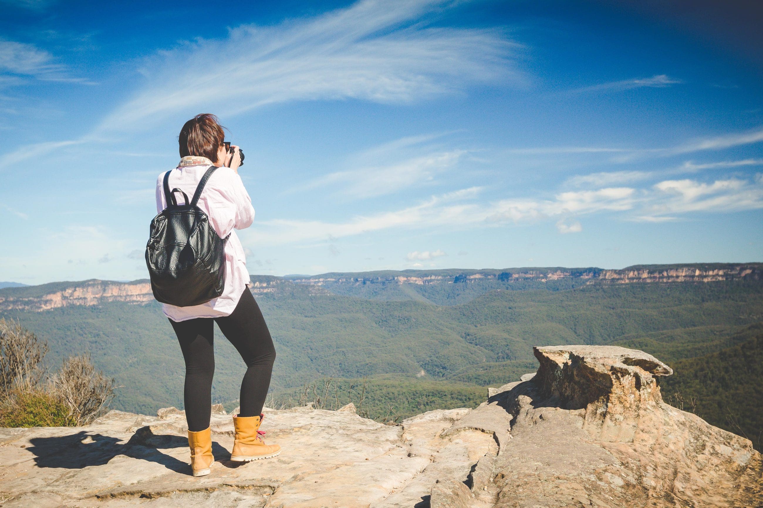Adventurer photographing breathtaking Blue Mountains scenery from a cliff on an Uncharted Tour, blue sky in the background.