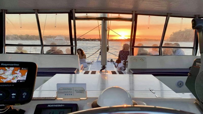 Stunning sunset view from catamaran cockpit on Sydney Harbour BYO Sunset Sparkle Cruise, guests relaxing and enjoying skyline.