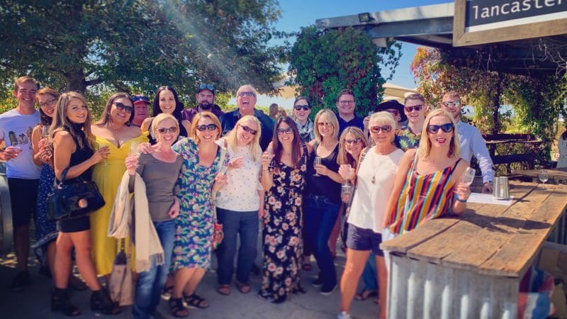 Happy group enjoying wine and sunshine at rustic bar during Half Day Swan Valley Wine Tour, surrounded by scenic outdoor views.