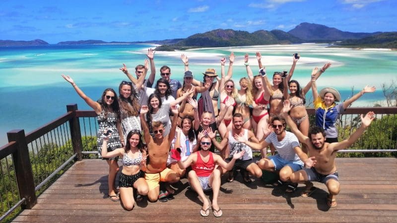 Happy young adults pose together on a deck with stunning turquoise Whitsundays water after an exciting Big Fury adventure tour.