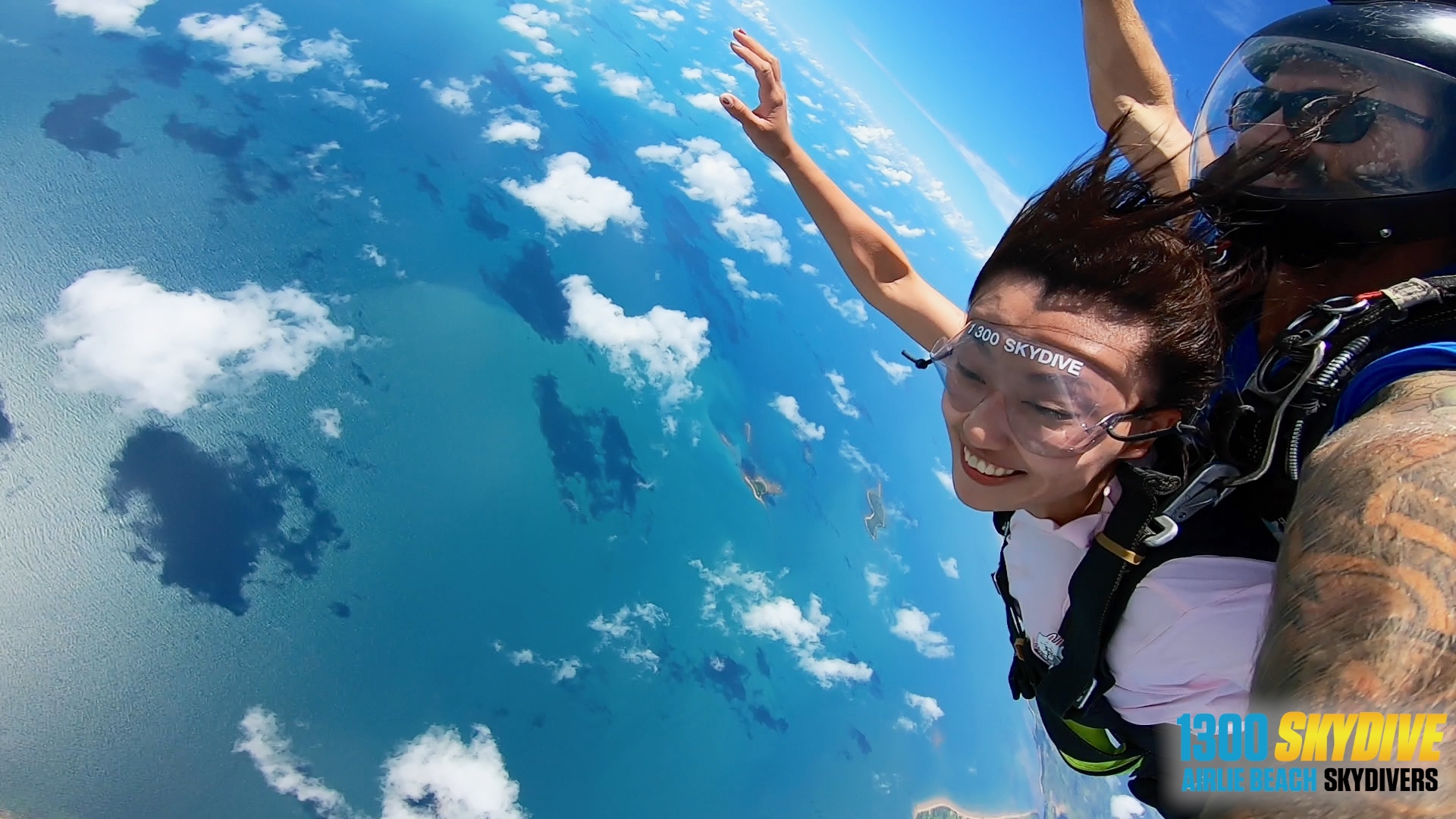 Woman tandem skydiving 15,000ft above the ocean at Airlie Beach, grinning with excitement, capturing an epic adventure mid-air.