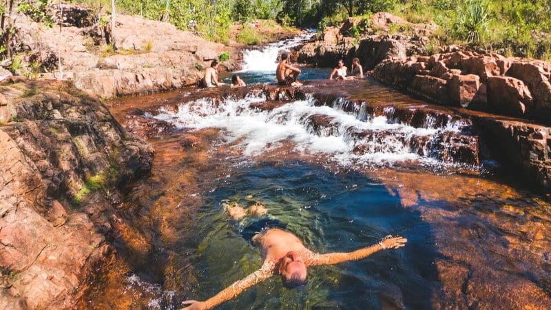 Visitors swim and unwind in a scenic rocky creek at Litchfield National Park, lush with greenery near Fogg Dam Wetlands, Australia.