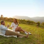 Couple enjoying premium wine on a scenic Hunter Valley tour, relaxing on a blanket with sweeping mountain views at sunset.