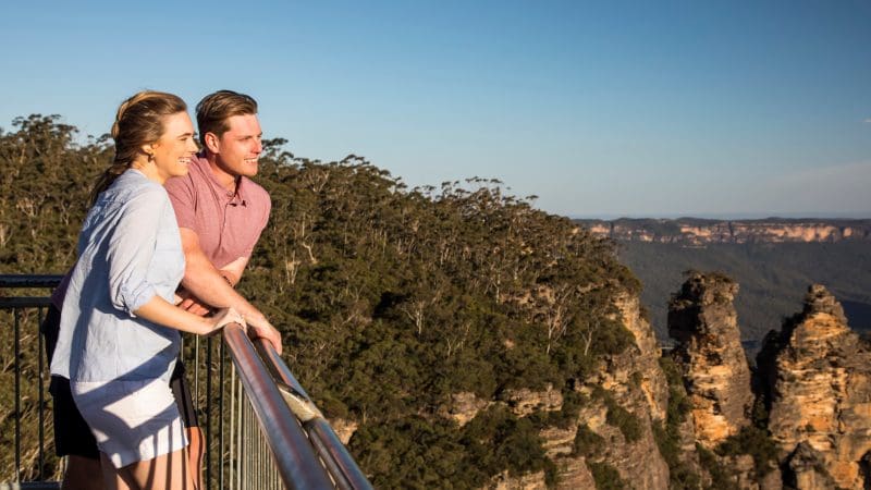 Happy couple admires stunning Blue Mountains sunset views on a 1 Day Wilderness Tour, clear sky above, perfect for adventure seekers.