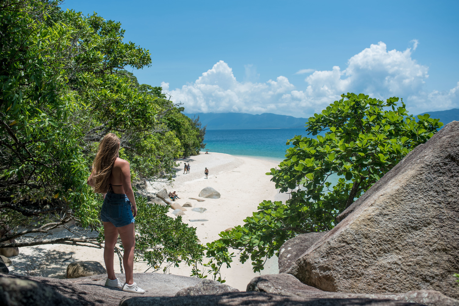 Woman standing on rocky shore gazing at Fitzroy Island, accessible via Half-day Tour Transfers with Fitzroy Island Ferries.