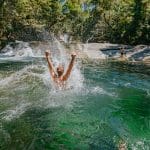 Adventurer plunging joyfully into a vibrant green river—discover this thrill on a top-rated 1 Day Waterfall and Rainforest Tour.