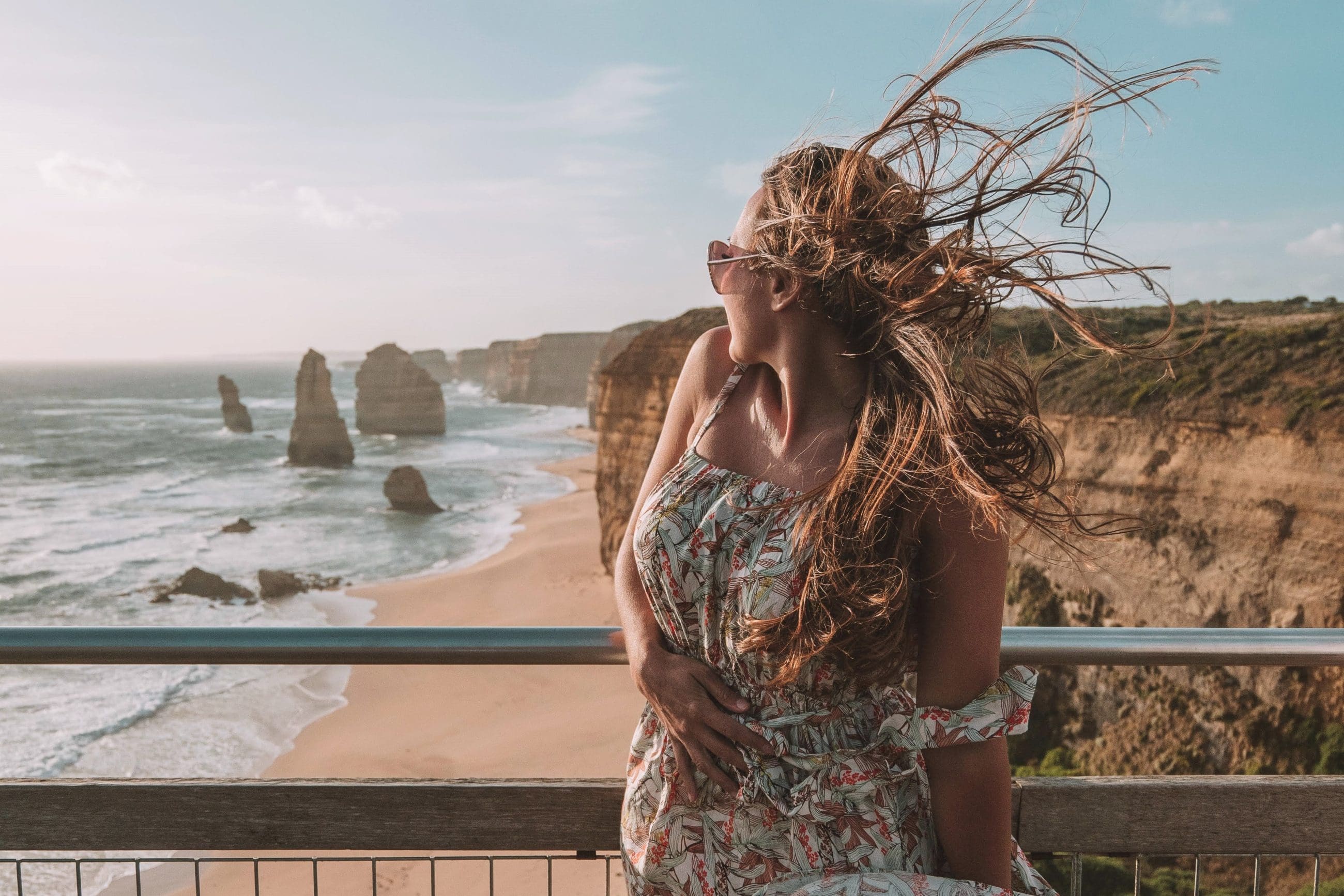 Woman with windswept hair enjoys panoramic cliff views along the Great Ocean Road during a 1 Day Reverse Eco Tour adventure.