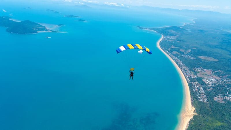 Experience breathtaking views as a skydiver with a yellow and blue parachute enjoys a 15,000ft tandem skydive over Mission Beach.