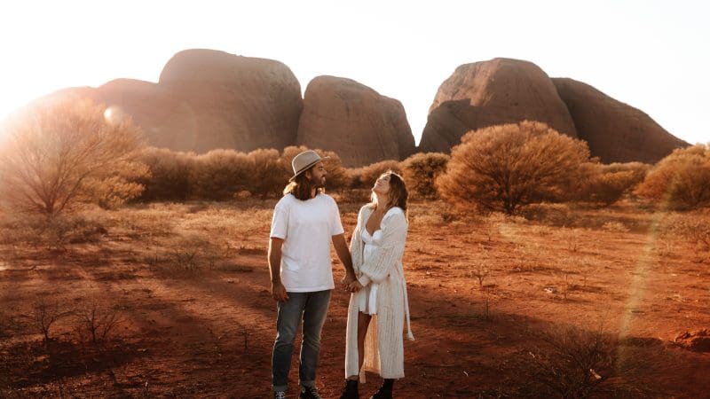 A couple holding hands among iconic Uluru Kata Tjuta desert rocks, bathed in sunlight on a 2-day tour from Ayers Rock Yulara.